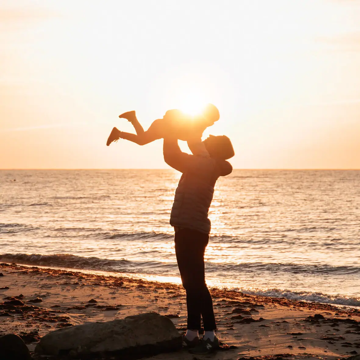 A woman holds a baby on the beach.