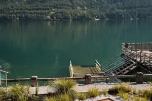 People in a swimming pool by a lake, with a mountain backdrop.