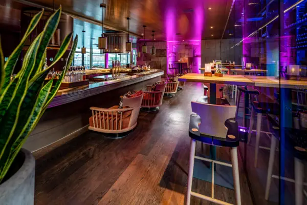 A bar with chairs and tables in a room with purple lights.