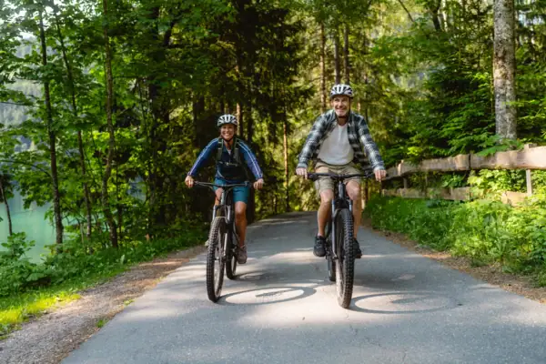 Bike tour A man and a woman are cycling along a path with trees.