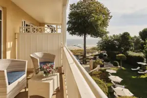 A balcony with chairs, a table and a tree.