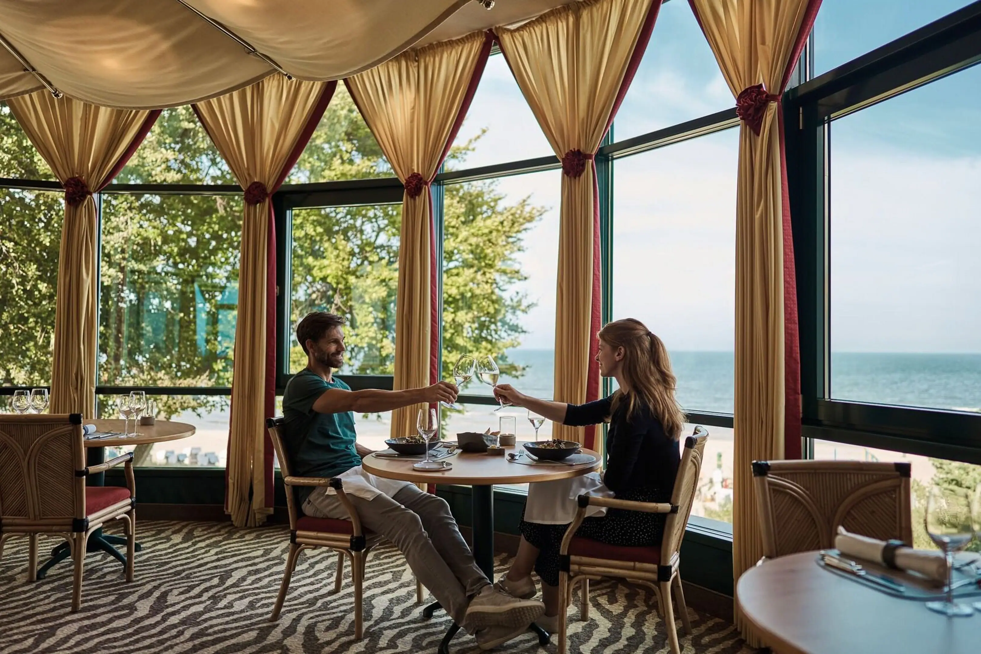 A man and a woman are sitting at a table with food in front of a large window.