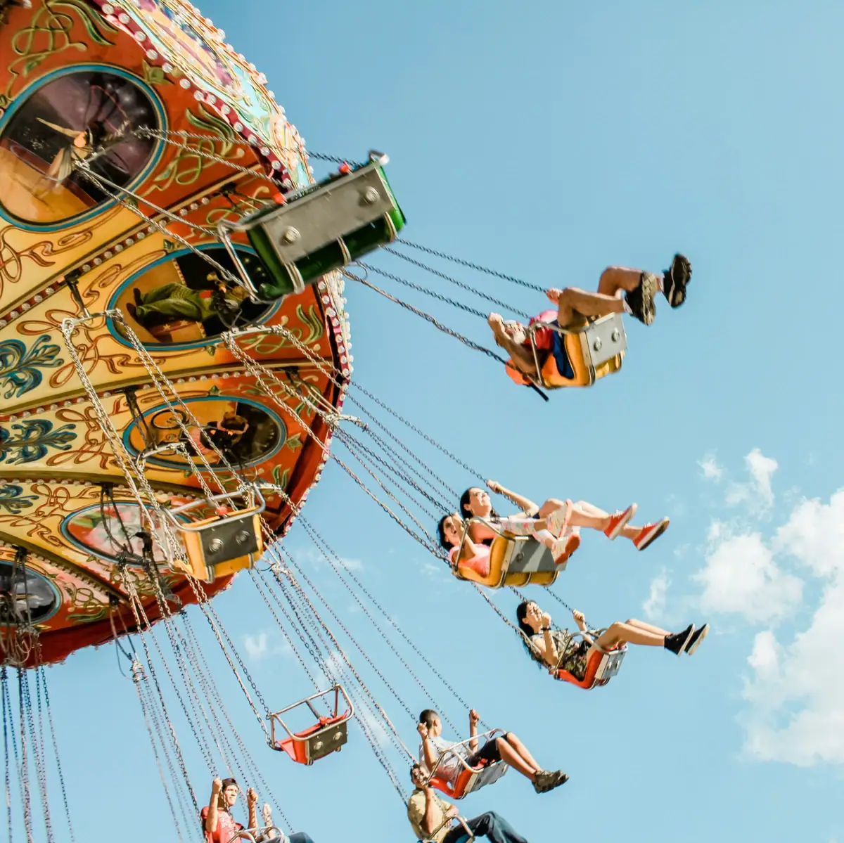 Cheerful children fly through the air in the seats of a chain carousel. The carousel has colourful patterns and the sky shines blue.