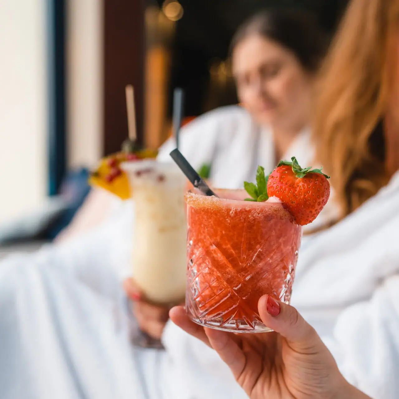 Cocktails Hand holds two drinks, one with a strawberry garnish.