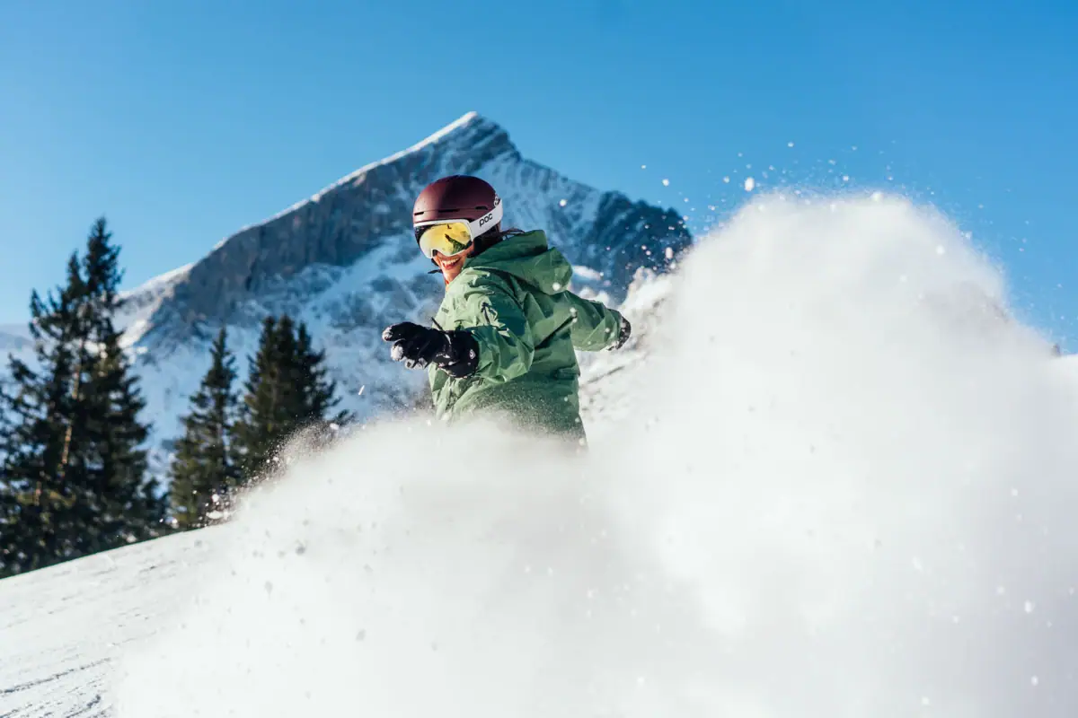 Snowboarder A person in a green jacket and helmet is skiing down a snowy mountain.