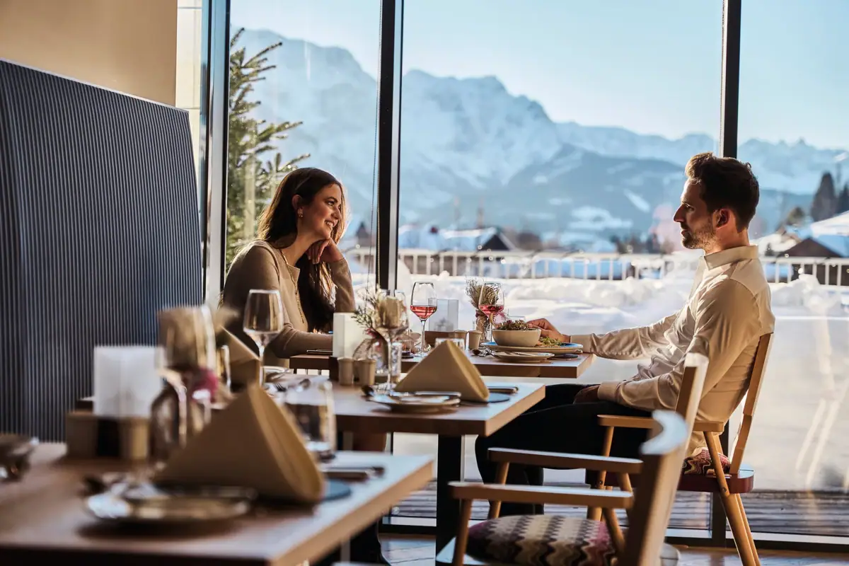 A man and a woman sit at a table with food and glasses of wine.