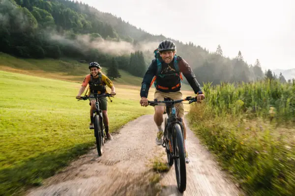 Two people are cycling on a dirt track.