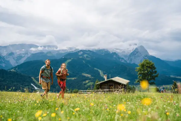 A man and a woman walk in a field with mountains in the background.