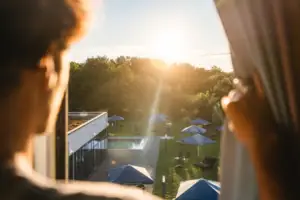 A person looks out over a pool with parasols and trees.
