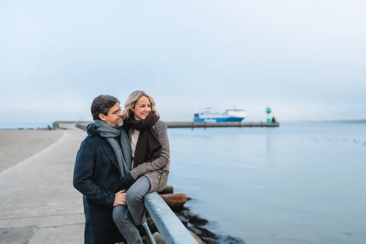 A man and a woman are standing by a railing by the water.