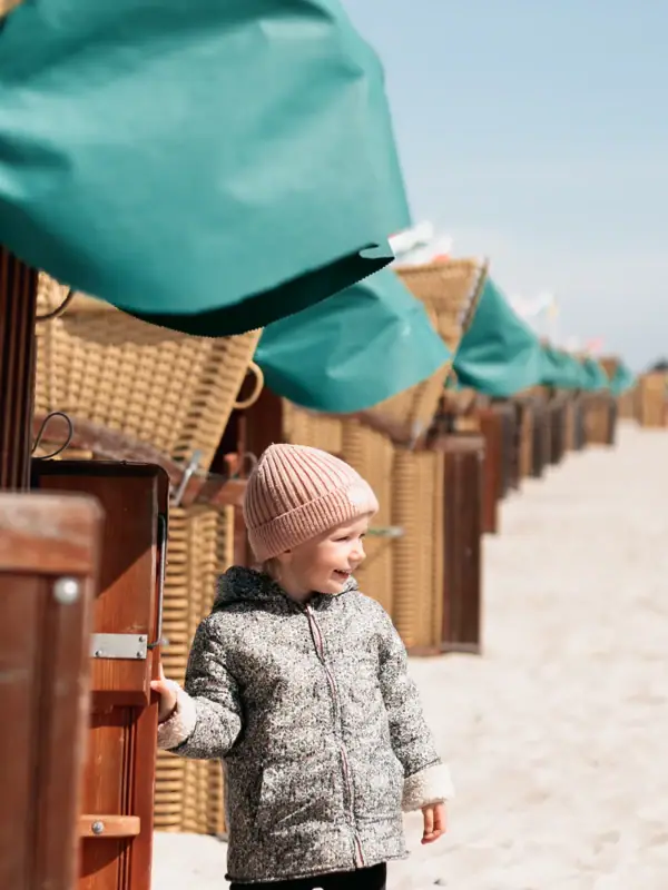 A child is standing in the sand next to a row of beach huts.