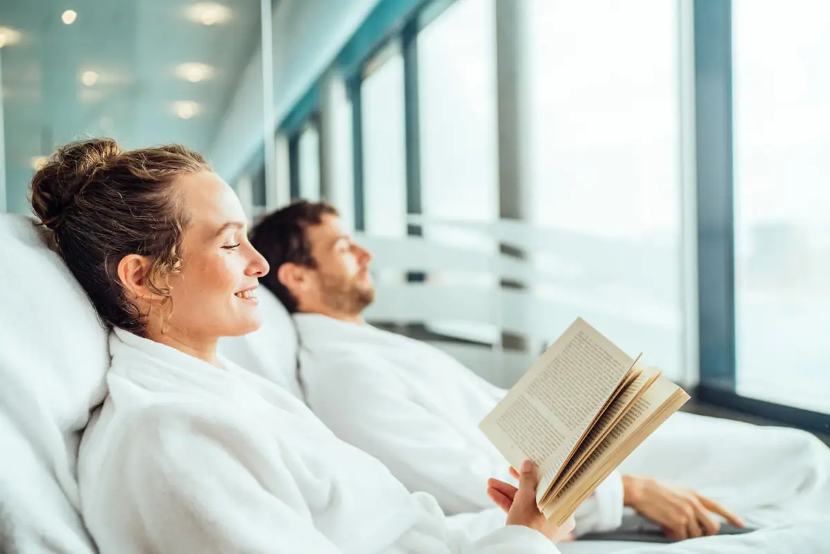 A man and a woman in bathrobes are reading a book.