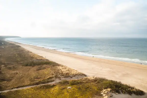 A beach with grass and sand under a cloudy sky.
