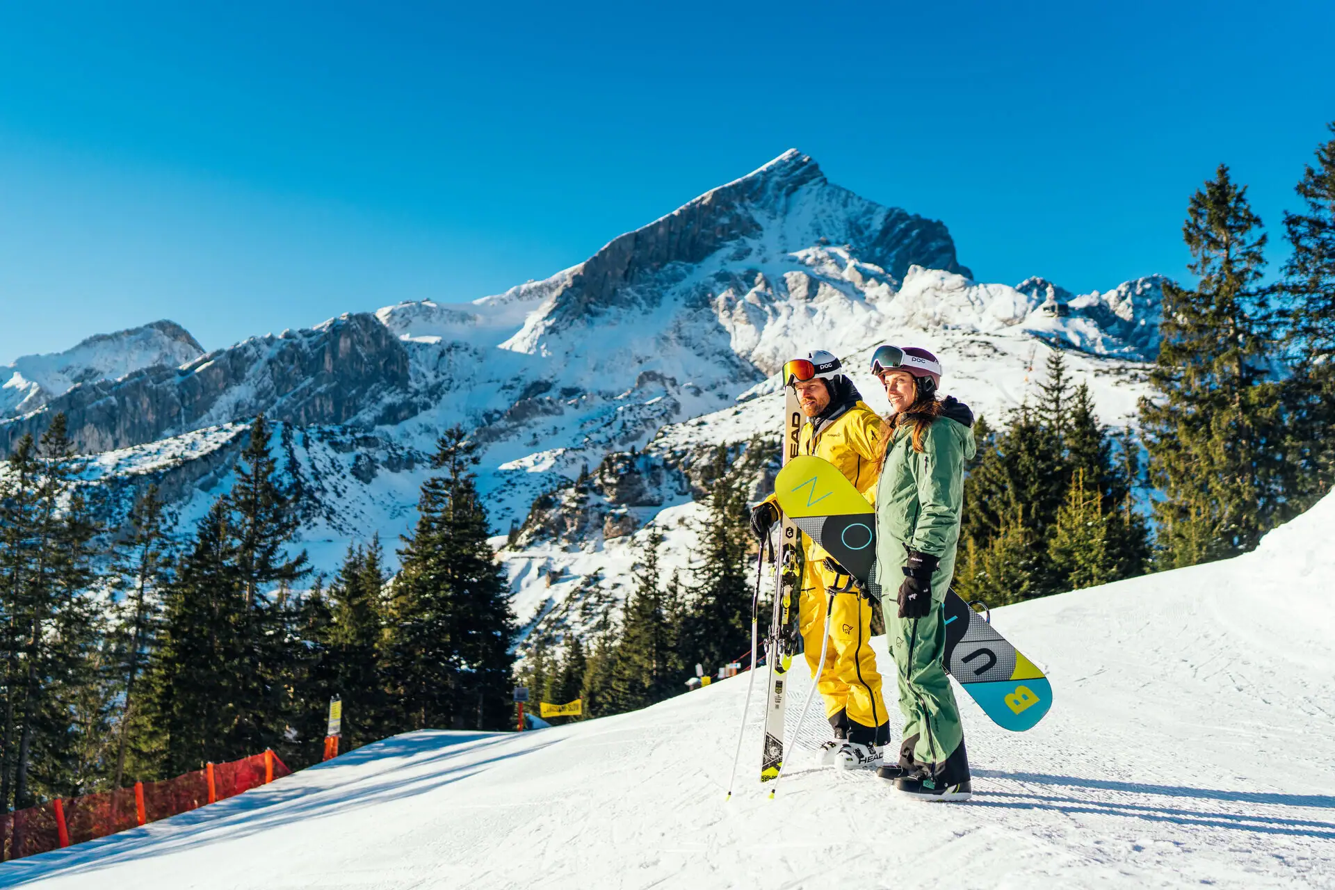Two people in snow clothing are standing on a snow-covered mountain.