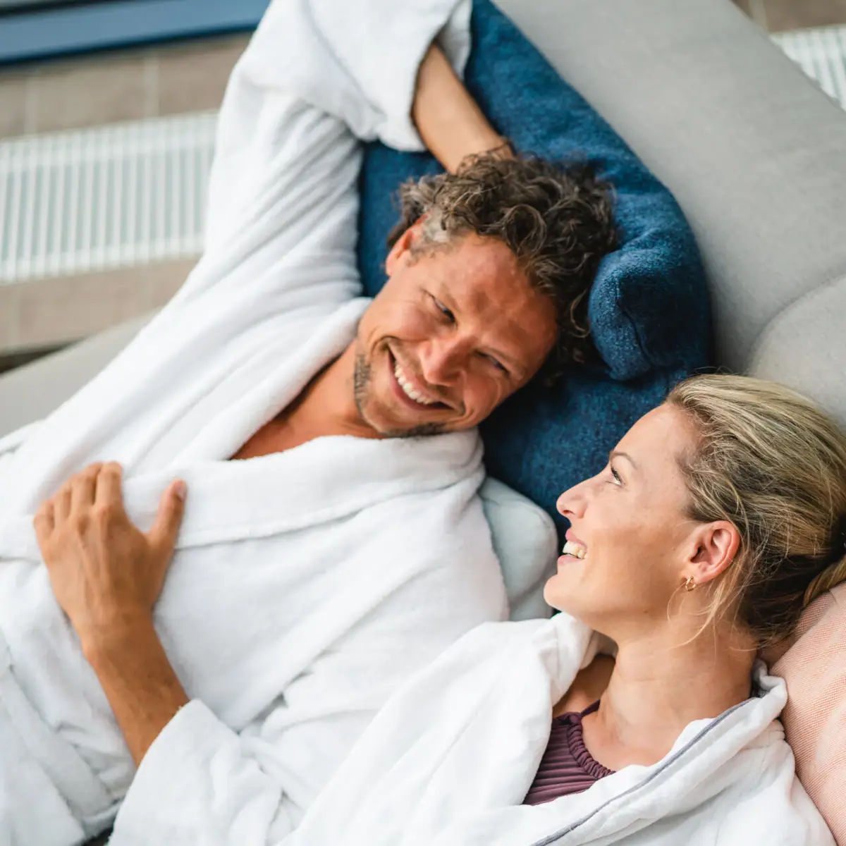 Couple in bathrobe A man and a woman lie smiling on a sofa.
