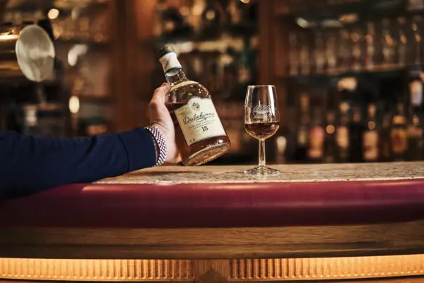 Whisky A hand is holding a bottle of alcohol next to a wine glass.