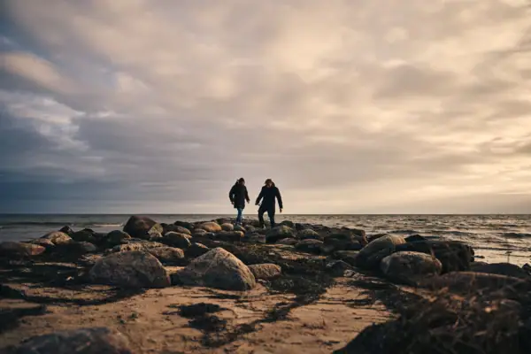 Two people are standing on a rocky beach.
