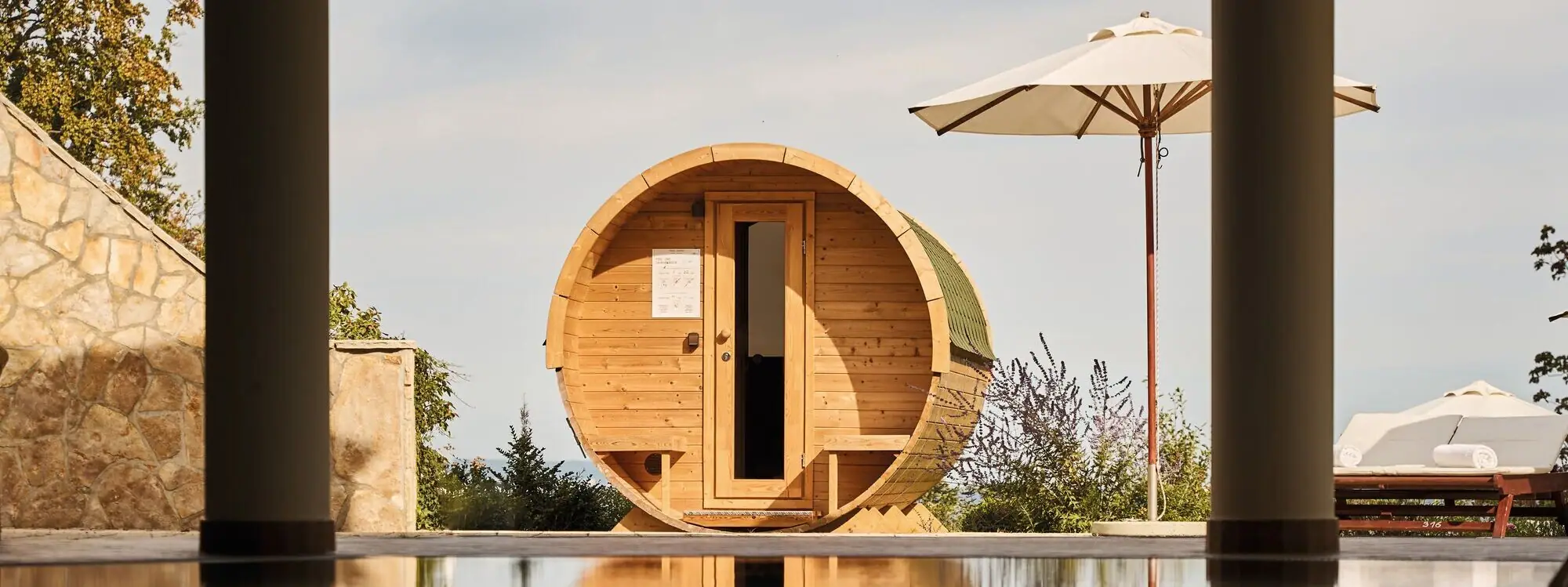 A wooden barrel-shaped sauna next to a reflecting pool.