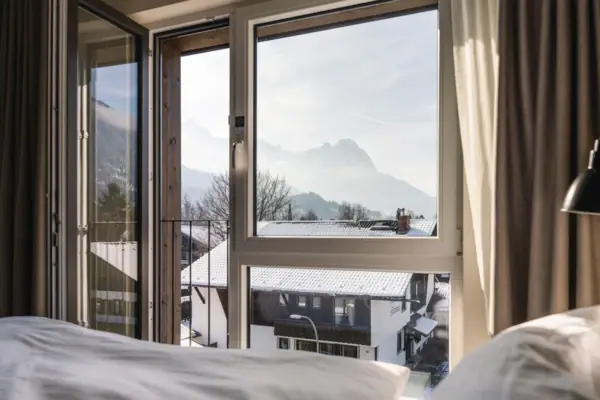 A hotel room at the aja Garmisch-Partenkirchen with a window and a view of the mountains.