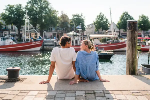 A man and a woman sit on a ledge and look at each other.