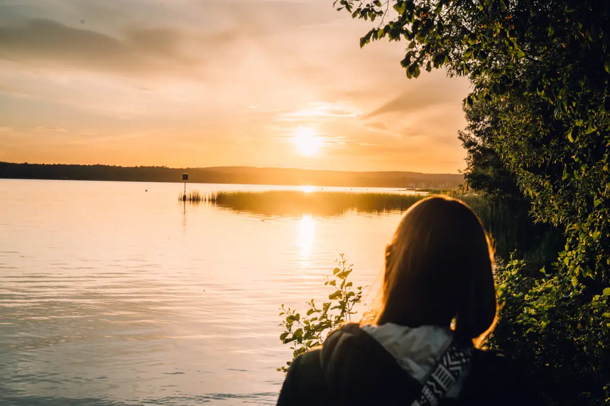 A woman gazes at the sunset over a body of water.