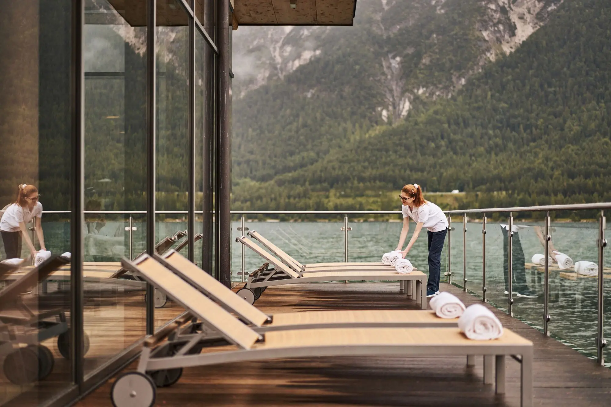 Woman laying towels on loungers on a terrace directly on Lake Achensee.