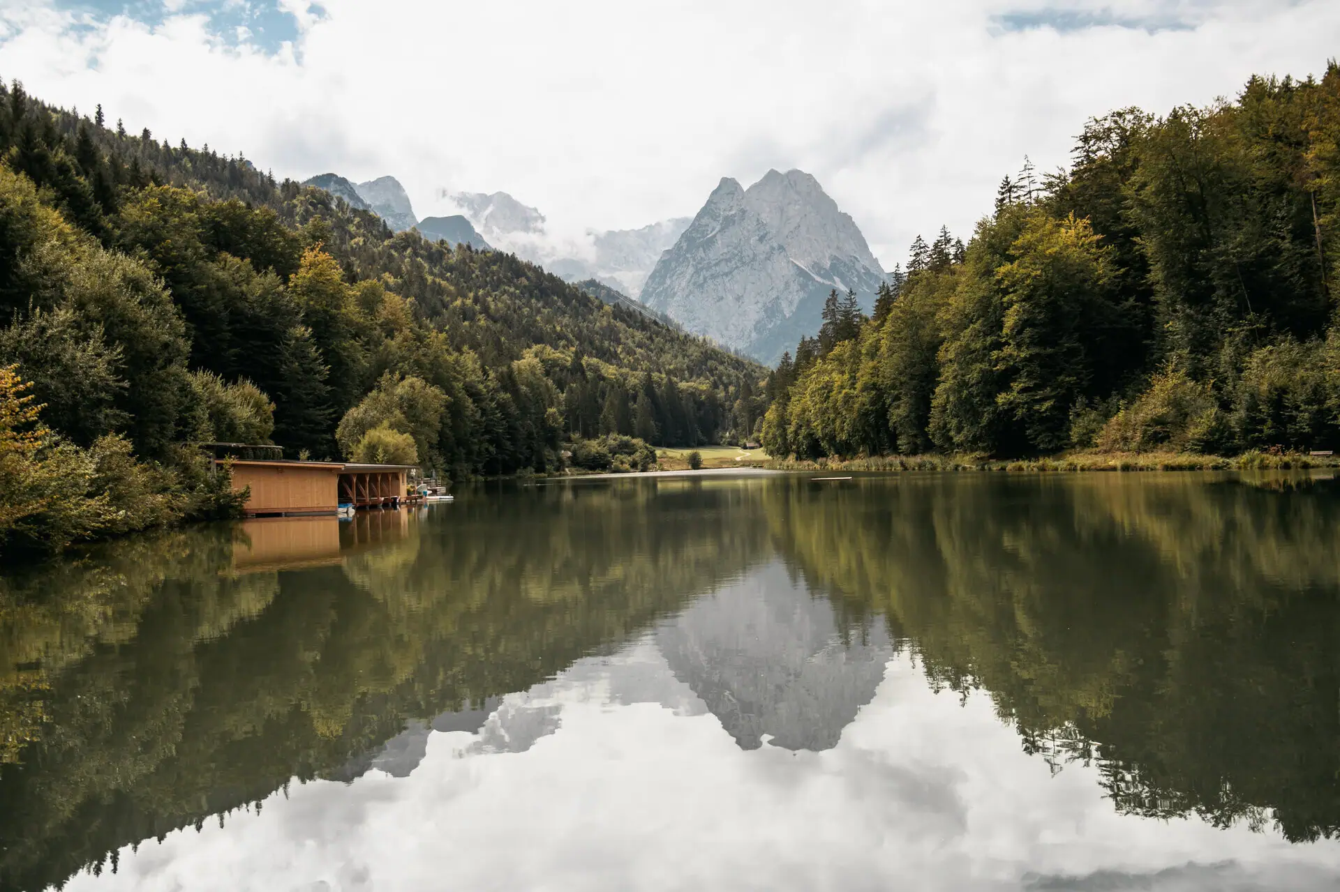 Riessersee A lake with a hut and mountains in the background.