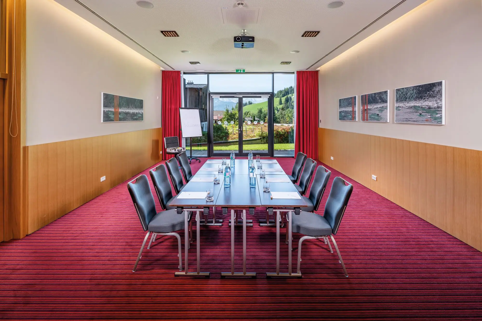 Conference room There is a long table in a conference room with a red carpet. Daylight floods in through a large patio door at the back.