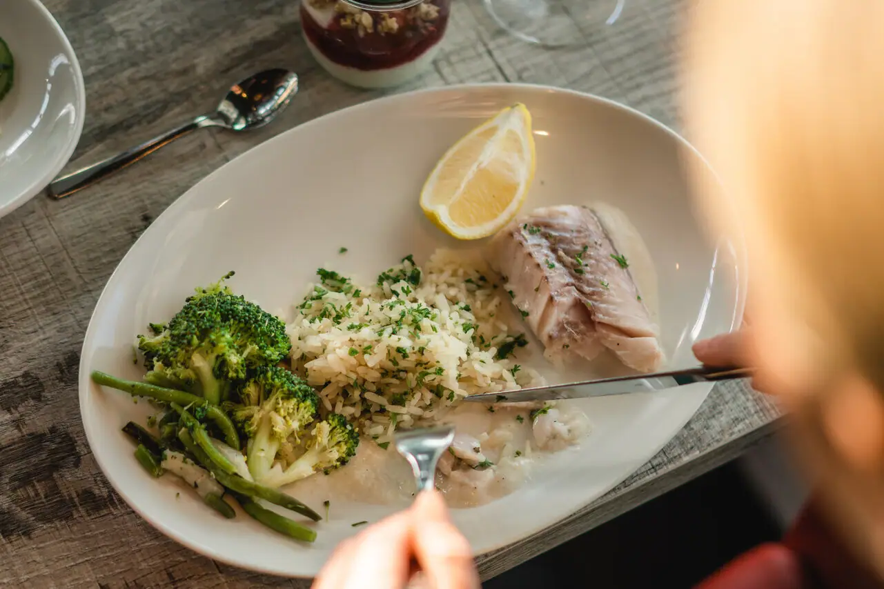 One person eats from a plate filled with broccoli, fish, lemon and rice.