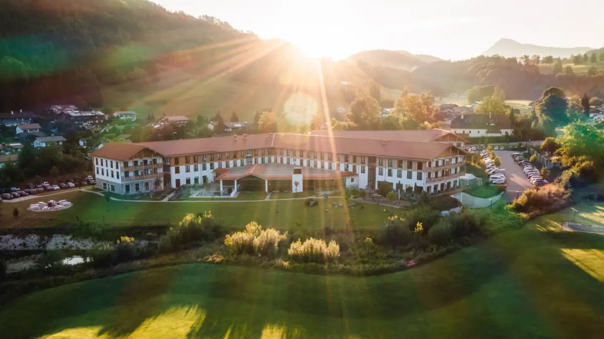 aja Hotel in Ruhpolding A large building with a large lawn in front of an outdoor pool in the foreground.