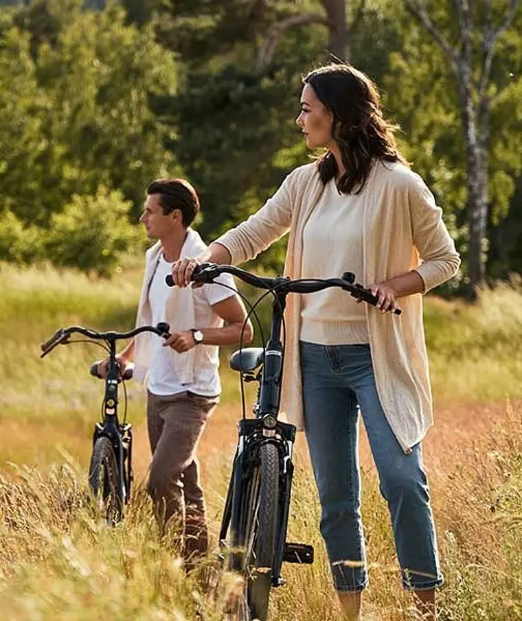 A man and a woman with bicycles are standing in a meadow.