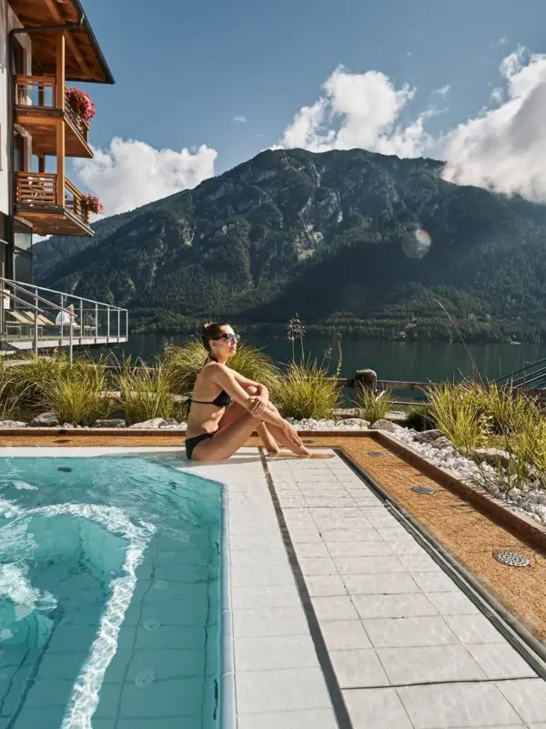 A woman sits by a pool with a mountain in the background.