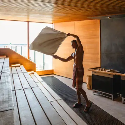 Sauna at aja Travemünde A man holds a towel in a sauna and gives a sauna infusion.