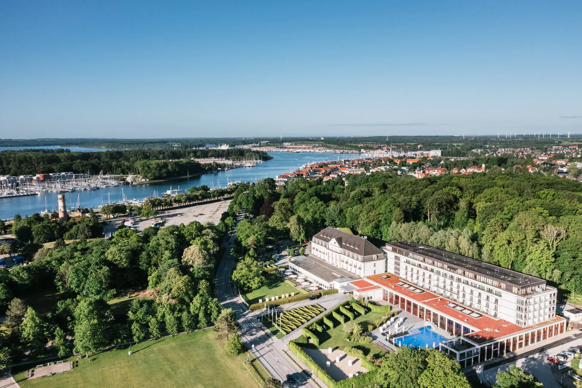 Large building with a pool surrounded by trees and water.