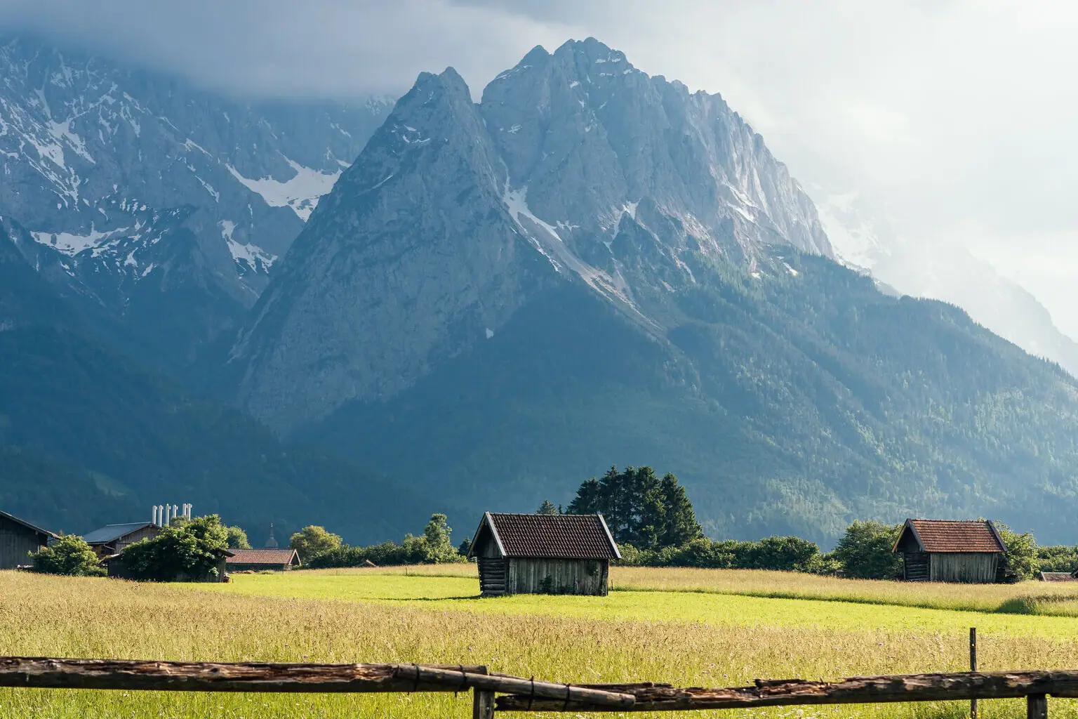 Alpspitzblick & Tegernauweg A wooden fence in a field with mountains in the background.