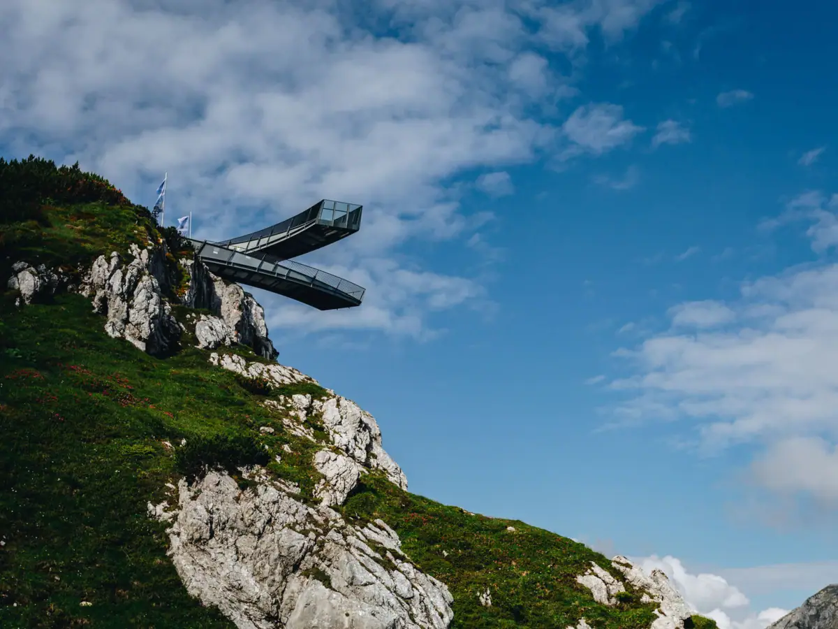 AlpspiX Bridge on a cliff with a cloudy sky in the background.