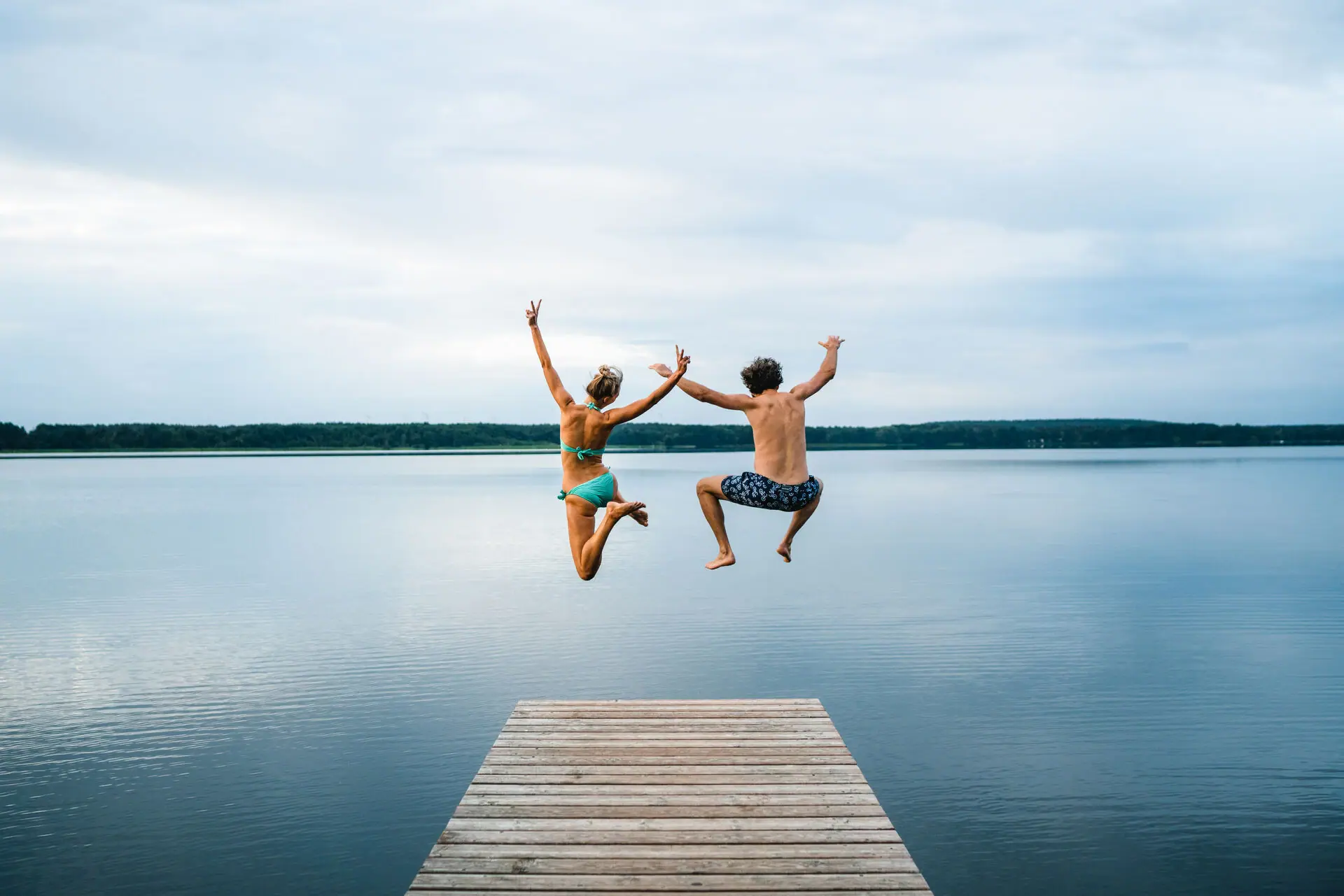 A man and a woman jump from a jetty into a lake.