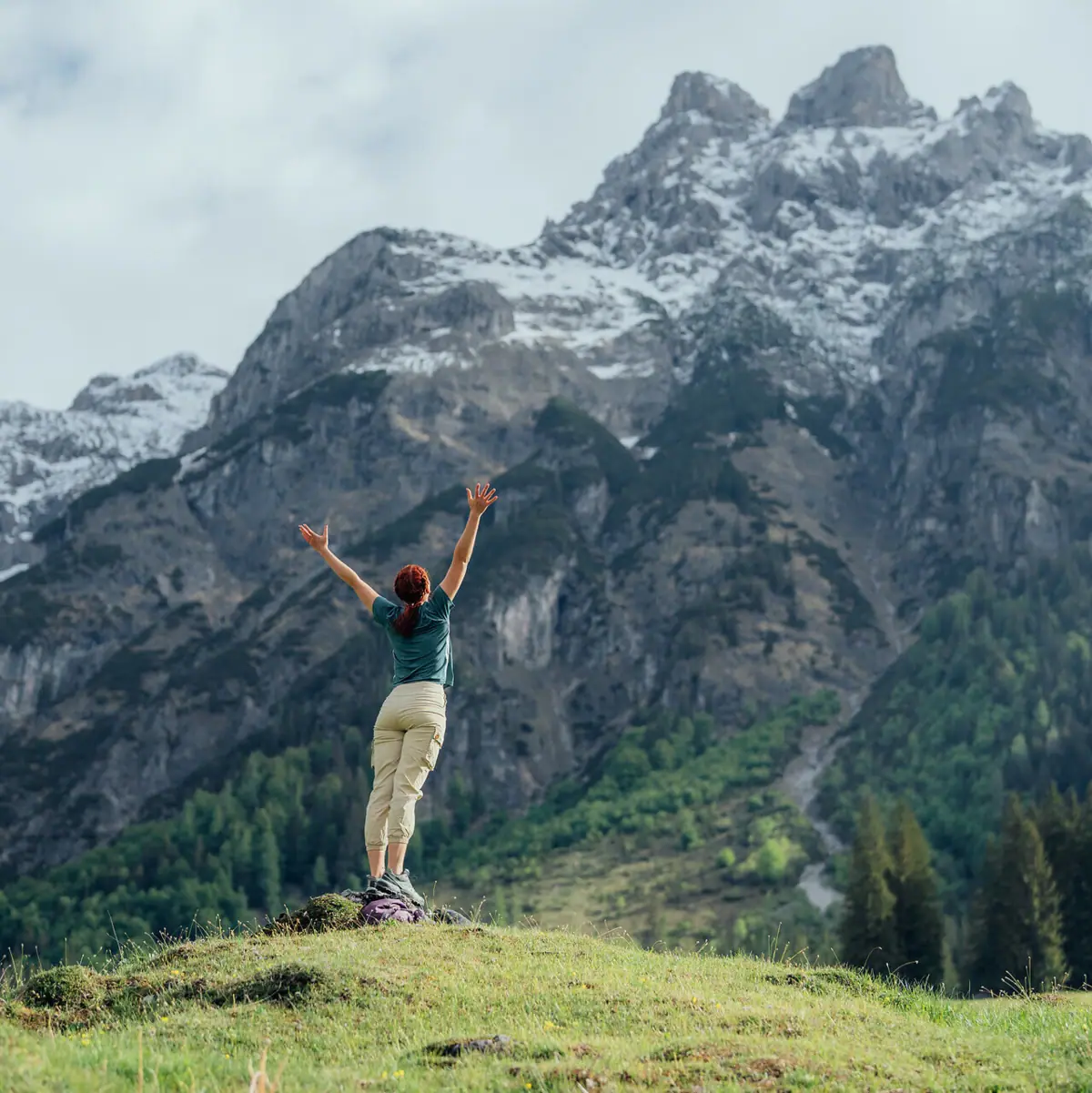 A woman is standing on a hill with her arms raised.