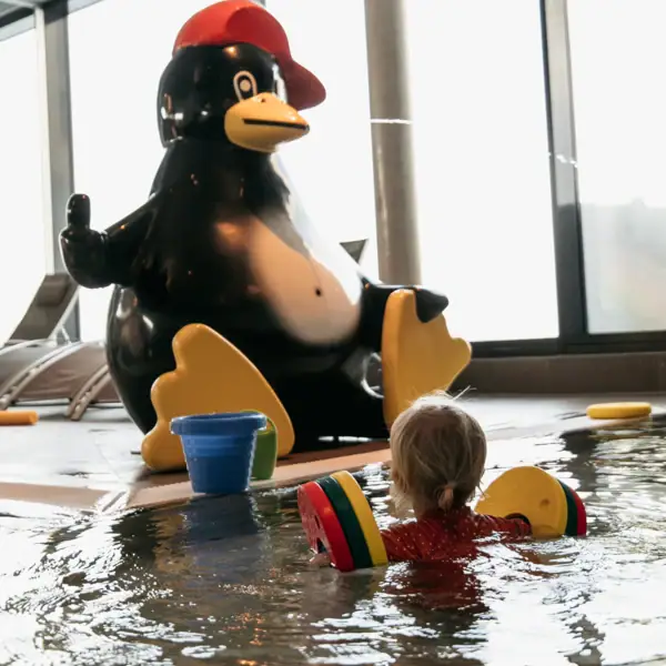 A child swims in a pool next to a penguin statue.