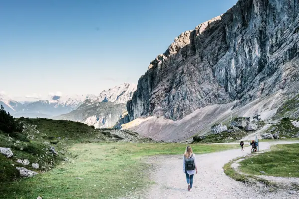 A woman walks along a path with a large mountain in the background.