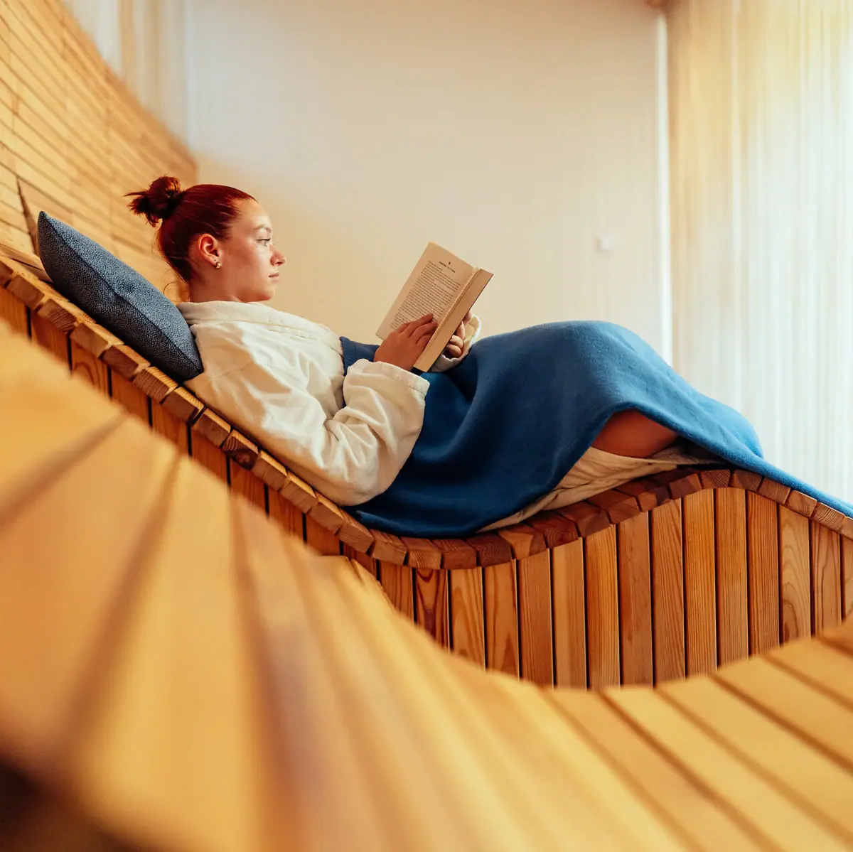 A woman is reading a book on a wooden bench.