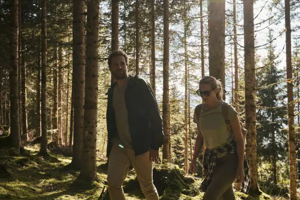 A couple walks through a forest. The animal sun is shining through the pine crowns and bathes the picture in warm colours.