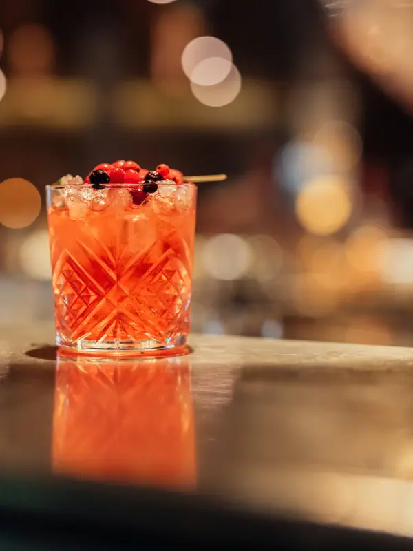 A glass containing a cocktail, garnished with berries.
