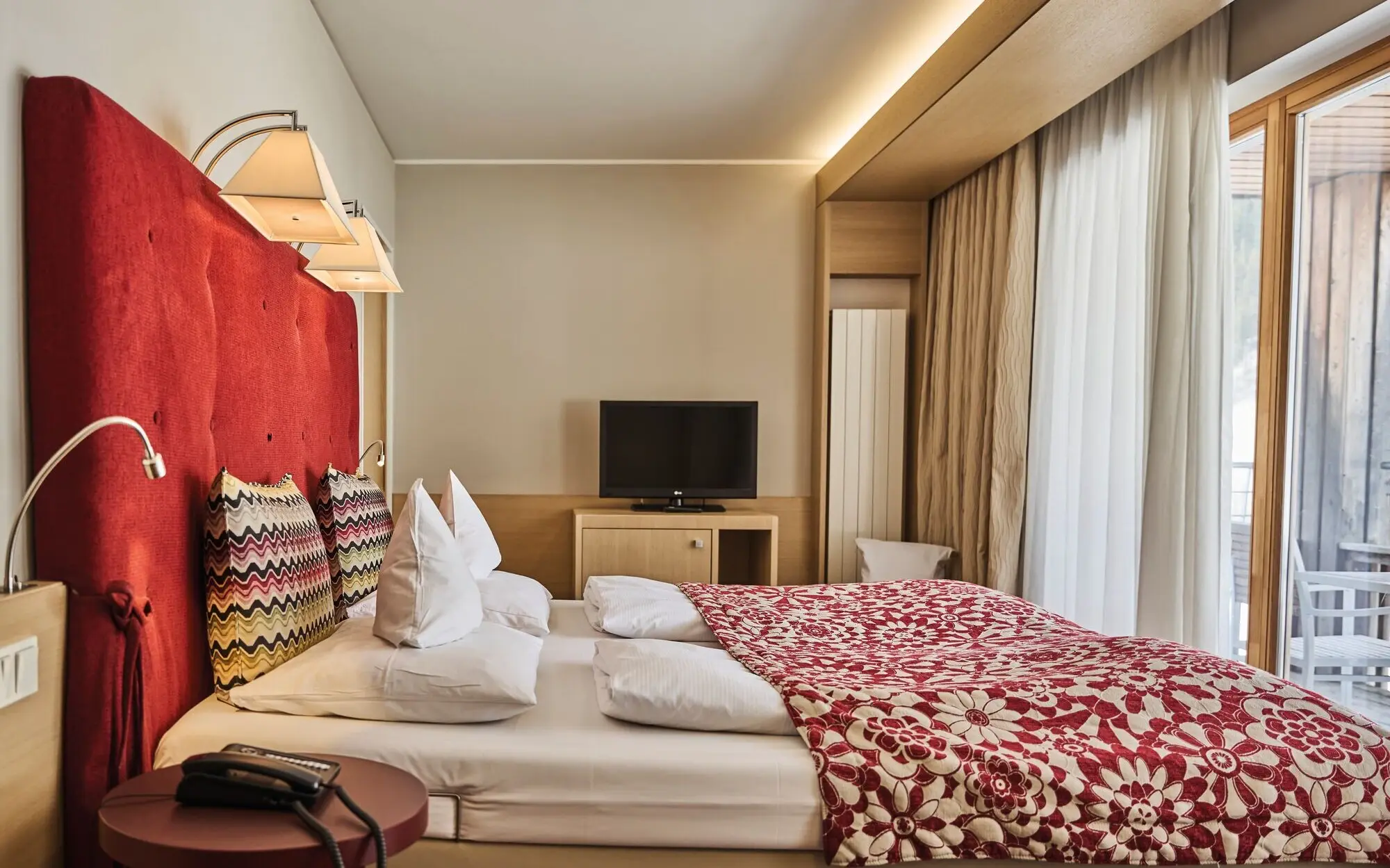 A bed with a red and white blanket and a TV in one room.