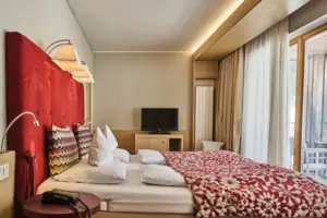 Bedroom Bed with a red and white blanket and a television in the background.