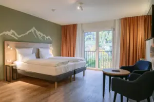 A room with a bed and chairs by a window overlooking the countryside.