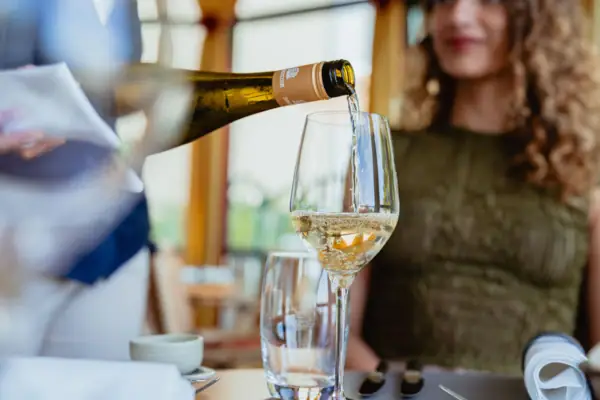 A waitress pours wine into a wine glass at a table in a restaurant.