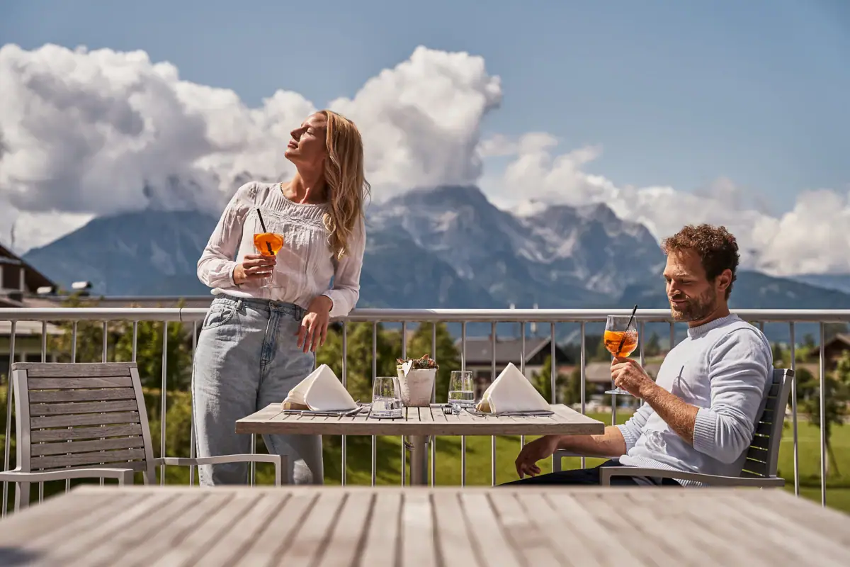 A man and a woman drink from a glass on a terrace.