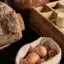 A small basket with breakfast eggs stands next to a bread basket and a wooden crate.