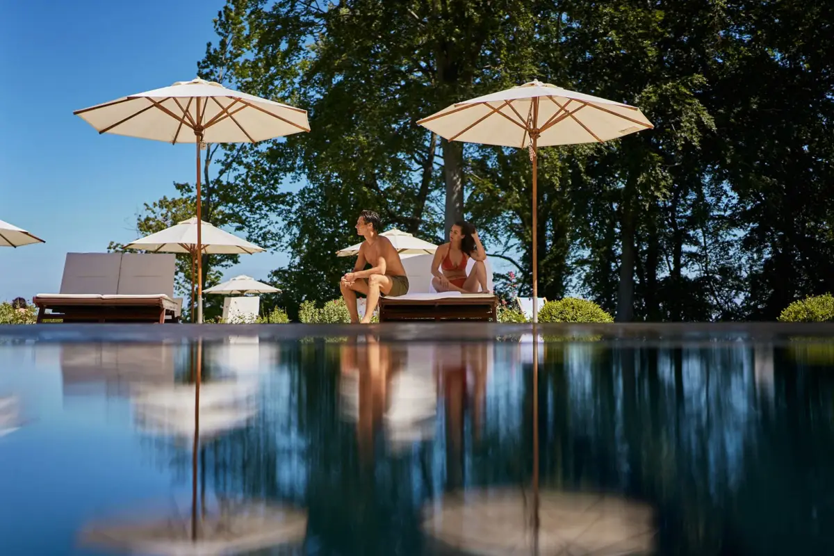 Panorama indoor pool A man and a woman sit at the edge of the pool with parasols.